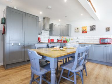 A kitchen with gray cabinets, wooden table with blue chairs, red appliances, and wall art at Escape To The Chapel Anglesey Bryngwran near Rhosneigr