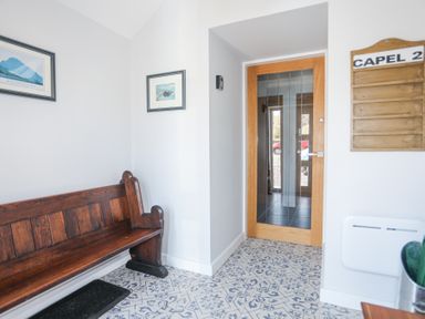 A small entryway with a wooden bench two framed pictures a wooden door with glass panels and a wooden signboard at Escape To The Chapel Anglesey Bryngwran near Rhosneigr