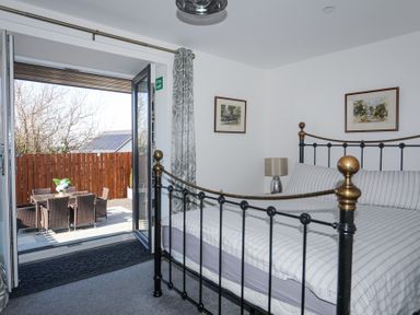 A bedroom with a black metal bed frame and striped bedding next to an open door leading to an outdoor patio with a table and chairs at Escape To The Chapel Anglesey