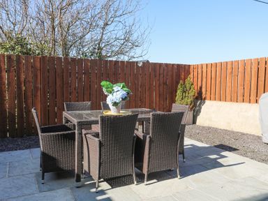 A patio area with a glass table and six woven chairs next to a wooden fence at Escape To The Chapel Anglesey Bryngwran near Rhosneigr