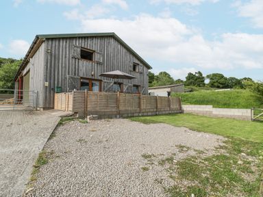 An exterior view of a wooden barn with fenced patio and gravel driveway at Top Lodge in Llanvair-Discoed near Penhow