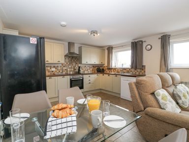 A kitchen with a glass dining table set with croissants orange juice and cups next to a sitting area with a sofa at Top Lodge Llanvair-Discoed near Penhow