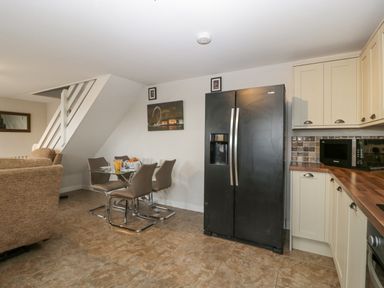 A kitchen and dining area with a black refrigerator a glass dining table with four chairs and beige cabinets at Top Lodge in Llanvair-Discoed near Penhow