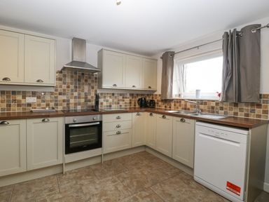 A kitchen with beige cabinets a tiled backsplash a window with curtains and various appliances at Top Lodge Llanvair-Discoed near Penhow