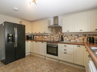 A kitchen with cream cabinets black refrigerator oven microwave kettle and tiled backsplash at Top Lodge Llanvair-Discoed near Penhow