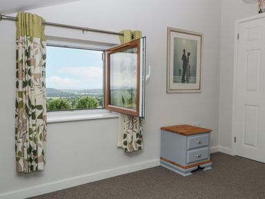 A room with an open window showing a landscape outside and a small drawer unit under a framed picture at Top Lodge in Llanvair-Discoed near Penhow