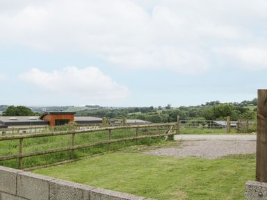 A fenced yard with grass and gravel driveway overlooking rolling hills and trees at Top Lodge in Llanvair-Discoed near Penhow