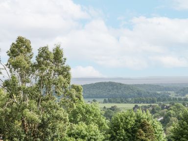 A landscape view of trees fields and hills under a partly cloudy sky at Top Lodge in Llanvair-Discoed near Penhow