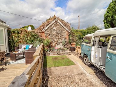 A garden area with wicker chairs and a wooden deck next to a stone wall and a parked van at The Old Post Office in Llanelian near Old Colwyn