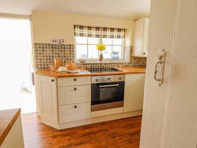 A kitchen with white cabinets a wooden countertop an electric stove a loaf of bread and a window with a checkered curtain at The Old Post Office in Llanelian near Old Colwyn