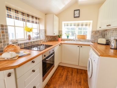 A kitchen with wooden countertops white cabinets and checkered blinds at The Old Post Office in Llanelian near Old Colwyn