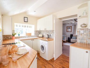 A kitchen with white cabinets wooden countertops washing machine and doorway to a sitting room at The Old Post Office in Llanelian near Old Colwyn