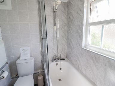 A bathroom with a toilet a bathtub with shower and a frosted window at The Old Post Office in Llanelian near Old Colwyn