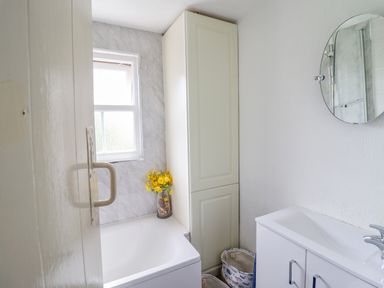 A bathroom with a bathtub yellow flowers a tall cabinet a round mirror and a white sink unit at The Old Post Office in Llanelian near Old Colwyn