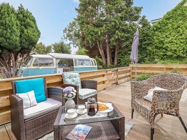 An outdoor wooden deck with wicker chairs a glass coffee table with coffee cups and croissants and a vintage blue and white van in the background at The Old Post Office in Llanelian near Old Colwyn
