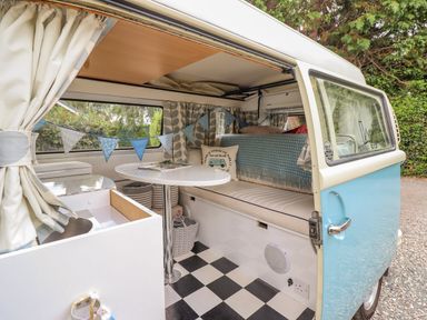 Interior of a camper van with a table, cushioned bench seating, curtains, bunting, and a kitchenette area at The Old Post Office in Llanelian near Old Colwyn