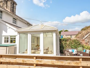 A glass conservatory attached to a white house with outdoor seating area and stone buildings in the background at The Old Post Office in Llanelian near Old Colwyn