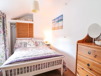 A bedroom with a bed a nightstand a dresser and a beach painting on the wall at The Old Post Office in Llanelian near Old Colwyn