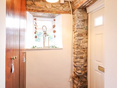 A small room with a white door stone wall wooden cabinets and a window with a lantern on the sill at The Old Post Office in Llanelian near Old Colwyn