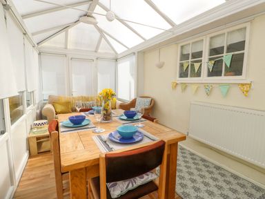 A dining area with a wooden table set with blue bowls and plates a sofa and armchair in a conservatory at The Old Post Office in Llanelian near Old Colwyn