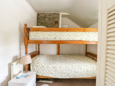 A bedroom with a wooden bunk bed and a white bedside table with a lamp at The Old Post Office in Llanelian near Old Colwyn