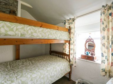 A bedroom with wooden bunk beds and a window with curtains and a small mirror at The Old Post Office in Llanelian near Old Colwyn