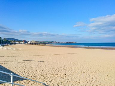A sandy beach with a pier and buildings in the background at The Old Post Office in Llanelian near Old Colwyn