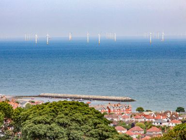 A coastal town with houses and trees facing a sea with an offshore wind farm at The Old Post Office in Llanelian near Old Colwyn