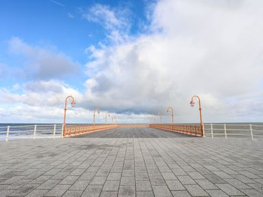 A paved walkway leading to a pier with orange railings and lamp posts extending into the sea at The Old Post Office in Llanelian near Old Colwyn