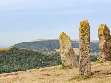Three tall standing stones on a hill with forested hills in the background at The Old Post Office Llanelian near Old Colwyn