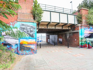 A pedestrian underpass with brick walls and metal beams with murals on the walls by the seaside at The Old Post Office in Llanelian near Old Colwyn