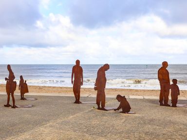Rust-colored metal statues of people on a beach promenade near the ocean at The Old Post Office in Llanelian near Old Colwyn