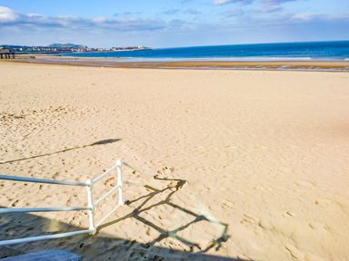 A sandy beach with a white railing in the foreground and ocean in the background at The Old Post Office in Llanelian near Old Colwyn