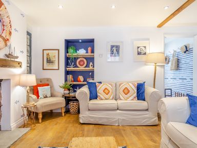 A living room with beige sofas and armchair with patterned cushions and a wooden floor at Pentreath in Kingsand