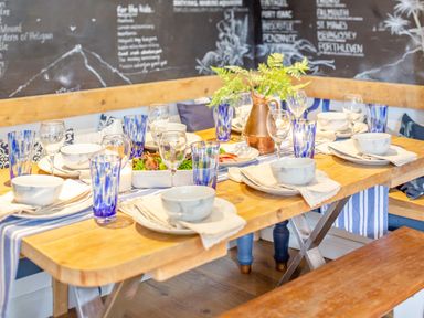 A dining table set with bowls glasses and blue striped table runner in a room with chalkboard walls at Pentreath in Kingsand