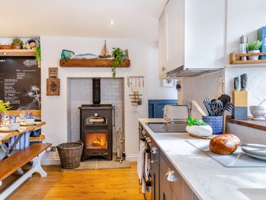 A kitchen with a wood burning stove and a countertop with kitchen utensils and bread at Pentreath in Kingsand