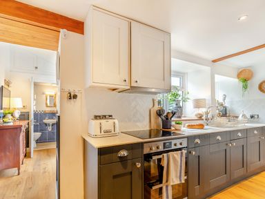 A kitchen with dark lower cabinets white upper cabinets a toaster oven an oven with tea towels a loaf of bread on the counter and a sink near a window at Pentreath in Kingsand