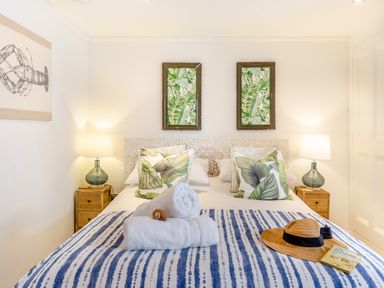 A bed with leaf patterned pillows and a blue striped blanket with rolled towels and a hat in a bedroom at Pentreath in Kingsand