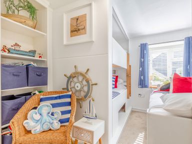A bedroom with bunk beds a wicker chair with an octopus cushion and a ship wheel on the wall at Pentreath in Kingsand