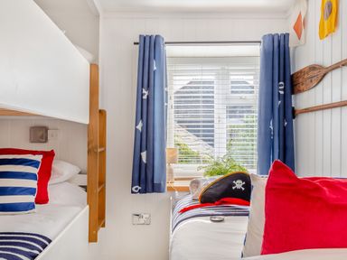 A bedroom with bunk beds pillows and a window with blue curtains and wooden oars on the wall at Pentreath in Kingsand
