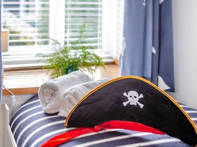 A pirate hat and rolled white towels on a striped blue and white blanket with a plant on a windowsill behind at Pentreath in Kingsand