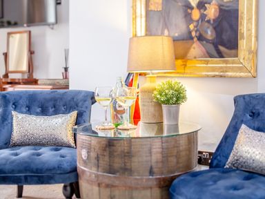A seating area with two blue chairs a round wooden table with a lamp plant and two glasses of wine at Pentreath in Kingsand