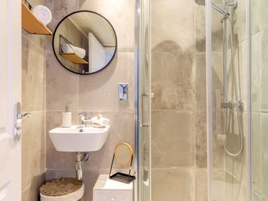 A bathroom with a wall-mounted sink a round mirror a small white cabinet and a shower enclosure at Pentreath in Kingsand