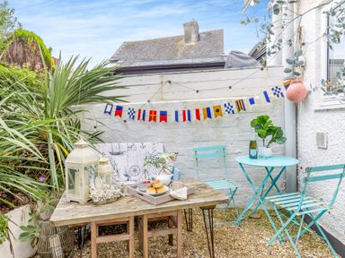 An outdoor patio area with a wooden table holding lanterns and food and turquoise metal chairs and table at Pentreath in Kingsand
