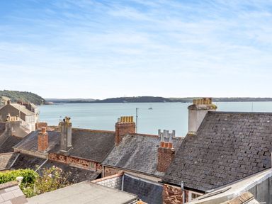 View of rooftops with chimneys overlooking a body of water with boats and distant land at Pentreath in Kingsand