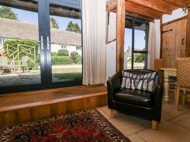 A sitting area with a black armchair with a pillow near glass doors and a window at Nympy Cottage in Nympsfield near Nailsworth