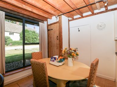 A dining area with a round table and two wicker chairs near a large window at Nympy Cottage in Nympsfield near Nailsworth