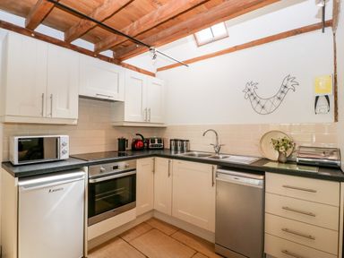 A kitchen with white cabinets black countertops a microwave fridge oven and dishwasher at Nympy Cottage in Nympsfield near Nailsworth