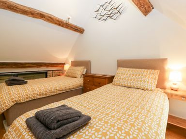 A bedroom with two single beds with yellow patterned bedding and wooden beams at Nympy Cottage in Nympsfield near Nailsworth