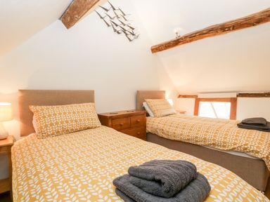 A bedroom with two single beds with yellow patterned bedding a wooden chest of drawers and exposed wooden beams at Nympy Cottage in Nympsfield near Nailsworth